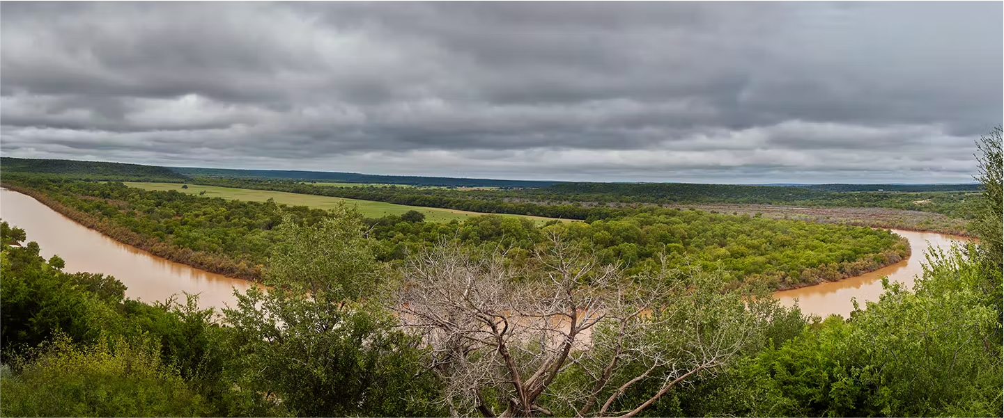Gran extensión de tierra con árboles, campos y cuerpo de agua.
